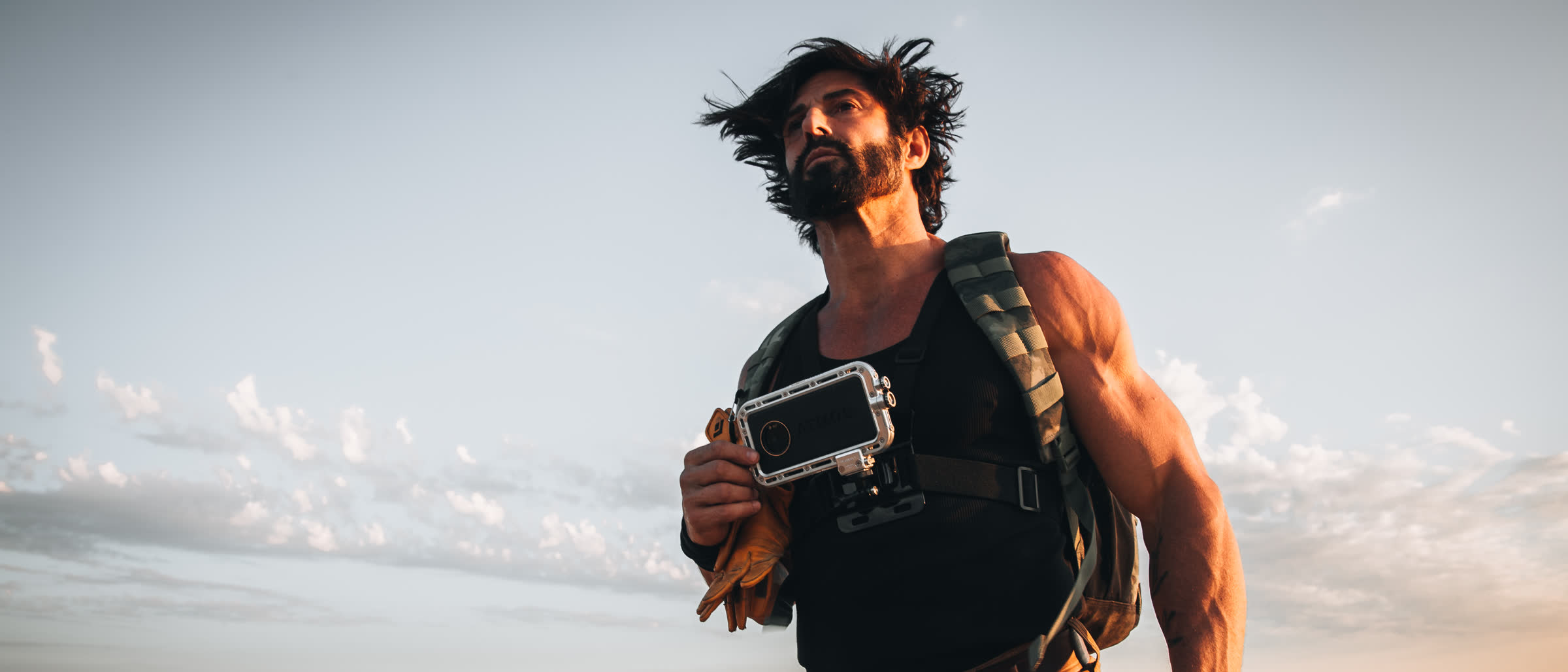 Man on a ridge at dusk holding a phone in an Atmos rugged waterproof case